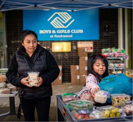 Person and child in front of a table full of food items at the CareOregon Boys & Girls Club at Rockwood.